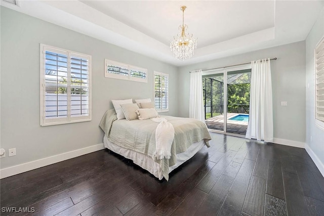 bedroom featuring a tray ceiling, dark wood finished floors, baseboards, a chandelier, and access to outside