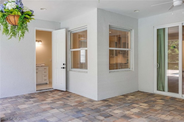 view of exterior entry with a ceiling fan, a patio, and stucco siding