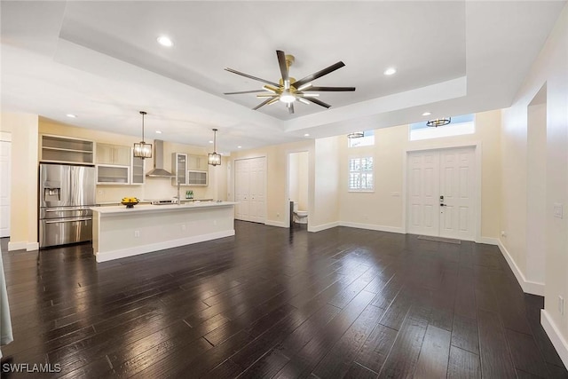 unfurnished living room with a ceiling fan, a tray ceiling, baseboards, dark wood-style flooring, and recessed lighting