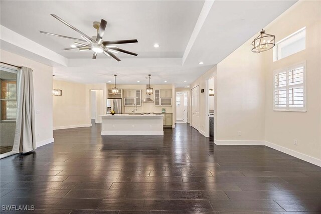 unfurnished living room with baseboards, recessed lighting, dark wood-type flooring, and ceiling fan with notable chandelier