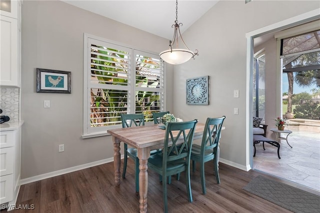 dining room featuring dark wood-type flooring, lofted ceiling, and baseboards