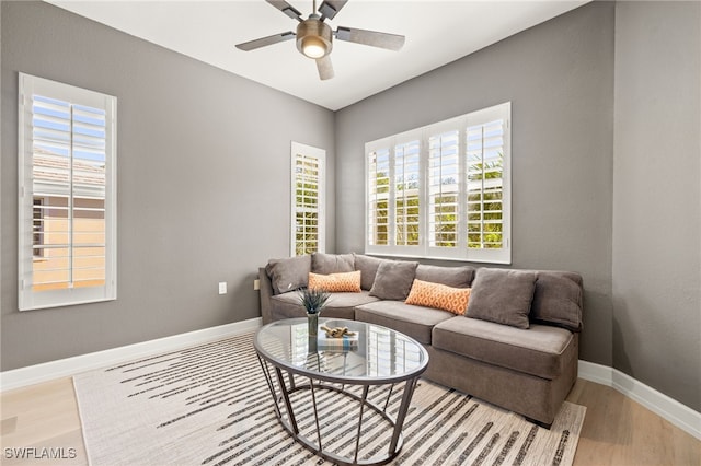 living room featuring baseboards, a ceiling fan, and light wood finished floors