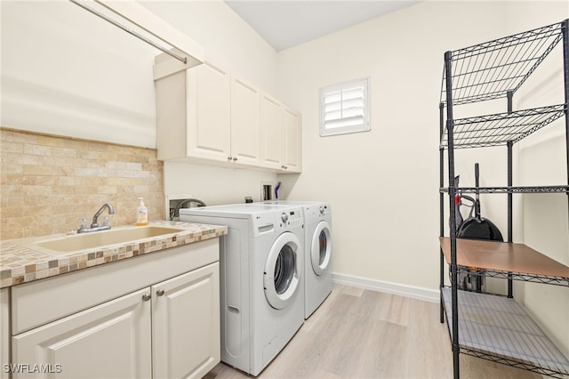 laundry area with baseboards, washer and clothes dryer, a sink, cabinet space, and light wood finished floors