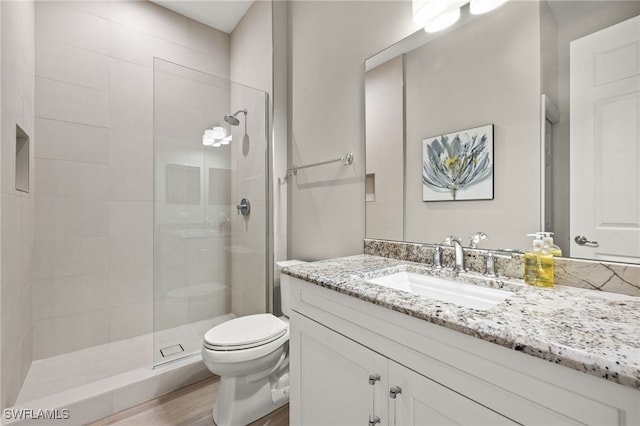 full bathroom with toilet, a tile shower, wood finished floors, and vanity