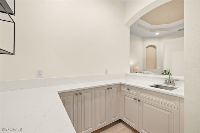 interior space featuring crown molding, arched walkways, a tray ceiling, light stone counters, and a sink