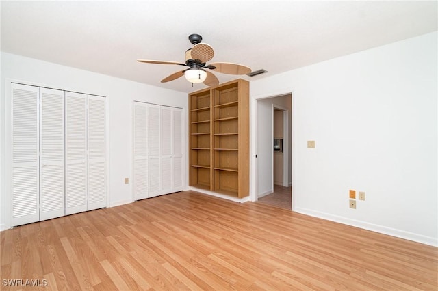 unfurnished bedroom featuring light wood-type flooring, baseboards, visible vents, and two closets