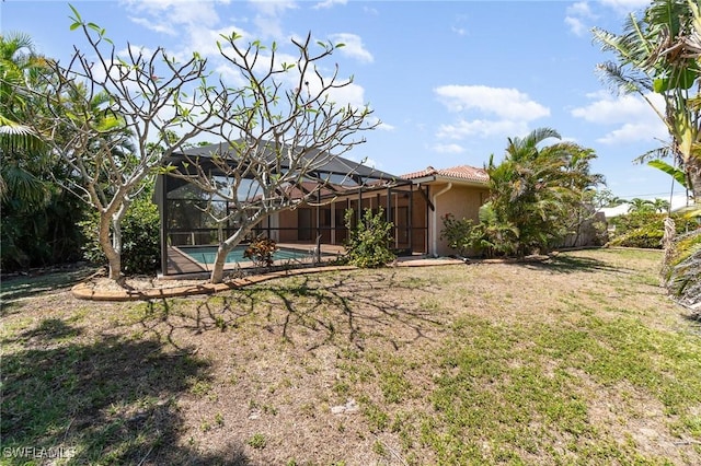 rear view of house featuring an outdoor pool, a tiled roof, stucco siding, a lawn, and a lanai