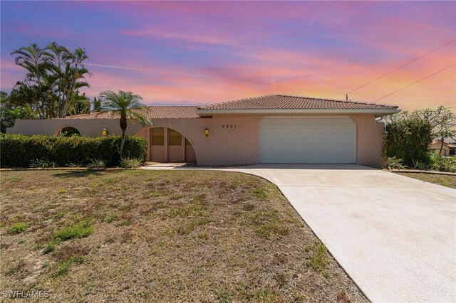 view of front of house with an attached garage, a tiled roof, driveway, and stucco siding