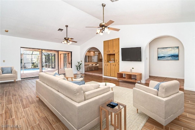 living room featuring light wood finished floors, arched walkways, vaulted ceiling, baseboards, and ceiling fan