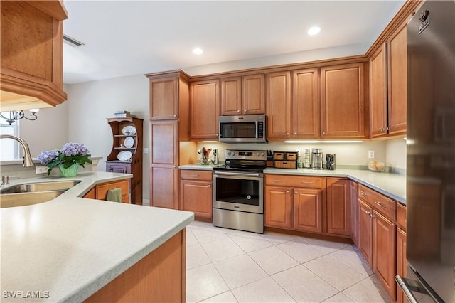 kitchen featuring appliances with stainless steel finishes, a sink, light countertops, brown cabinetry, and light tile patterned floors