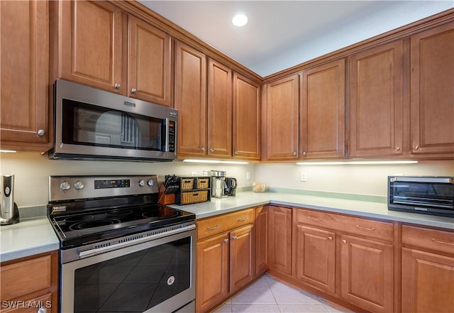 kitchen with brown cabinetry, light countertops, light tile patterned floors, and stainless steel appliances