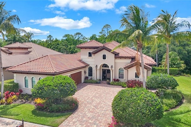 mediterranean / spanish-style house featuring stucco siding, decorative driveway, a tiled roof, and a garage