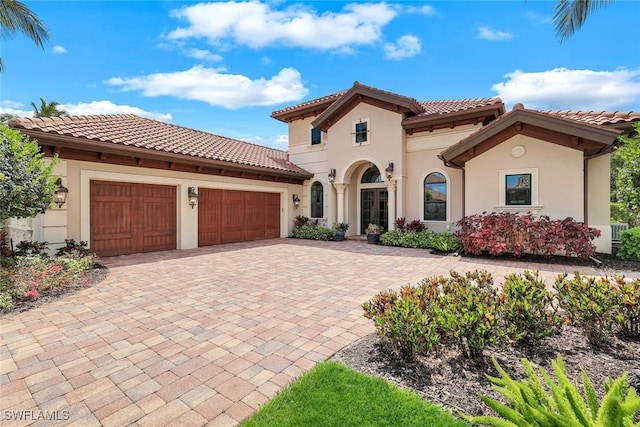 mediterranean / spanish-style home with a tile roof, decorative driveway, an attached garage, and stucco siding