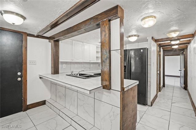 kitchen with a textured ceiling, white cabinetry, black refrigerator with ice dispenser, and marble finish floor