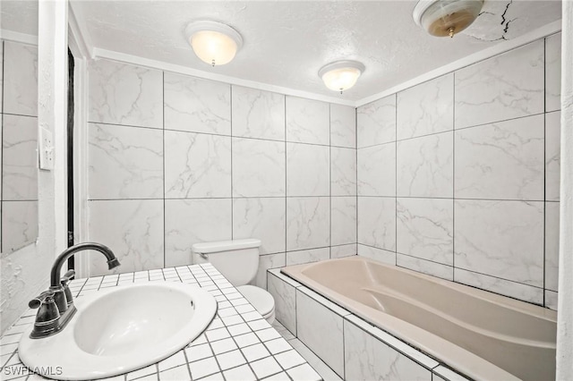 bathroom featuring tile walls, a tub to relax in, toilet, a sink, and a textured ceiling