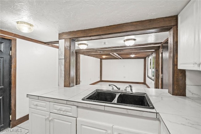 kitchen featuring baseboards, white cabinets, a textured ceiling, and a sink
