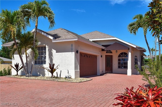 view of front facade with a garage, a shingled roof, stucco siding, and decorative driveway
