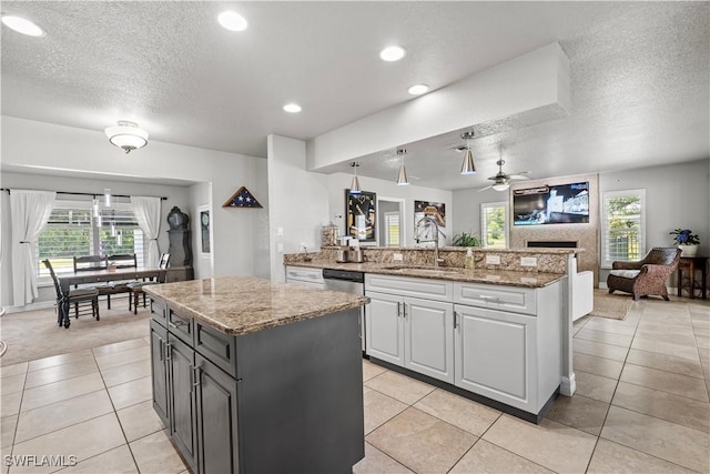 kitchen with stainless steel dishwasher, a center island, a sink, a textured ceiling, and open floor plan