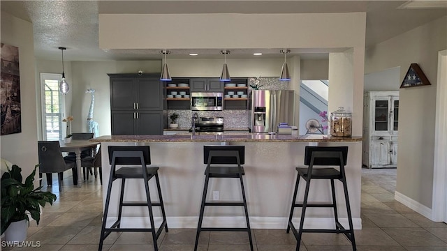 kitchen featuring backsplash, appliances with stainless steel finishes, tile patterned flooring, open shelves, and a breakfast bar area
