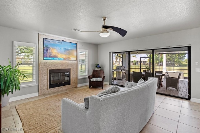 living area with a ceiling fan, a textured ceiling, light tile patterned flooring, a fireplace with flush hearth, and visible vents