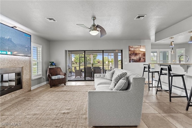 tiled living area with a glass covered fireplace, a ceiling fan, visible vents, and a textured ceiling