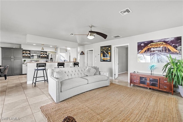 living room with baseboards, a ceiling fan, visible vents, and light tile patterned floors