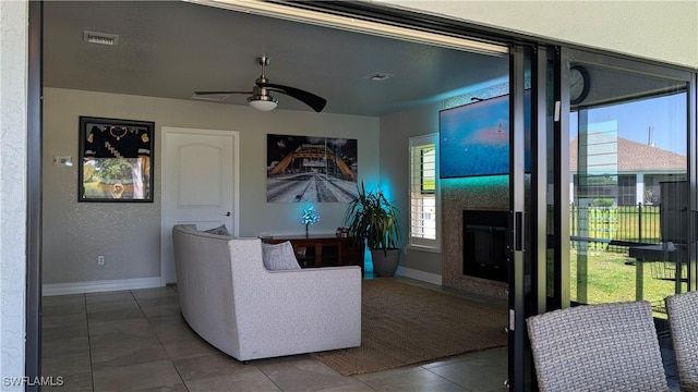 living area featuring a fireplace with flush hearth, ceiling fan, baseboards, tile patterned flooring, and visible vents