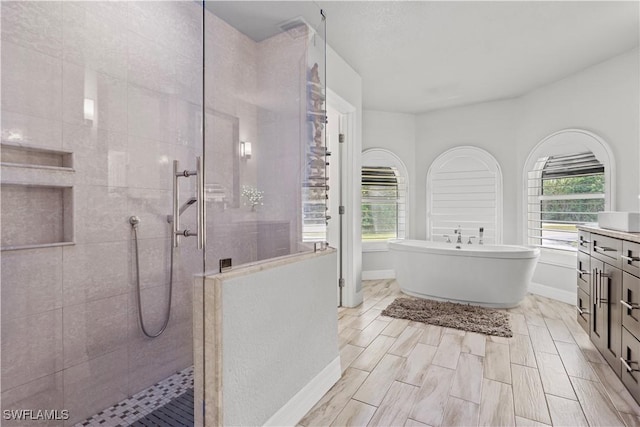 bathroom with a soaking tub, baseboards, walk in shower, and vanity