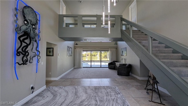 foyer featuring stairs, tile patterned flooring, baseboards, a high ceiling, and carpet flooring