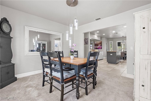 dining space featuring baseboards, visible vents, and light colored carpet