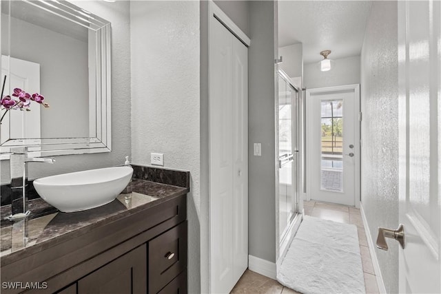 full bathroom with tile patterned floors, a stall shower, baseboards, a textured wall, and vanity