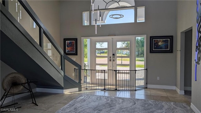tiled foyer entrance featuring a towering ceiling, french doors, baseboards, and stairs