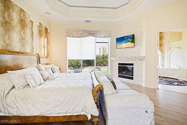 bedroom with crown molding, wood finished floors, a glass covered fireplace, and a raised ceiling