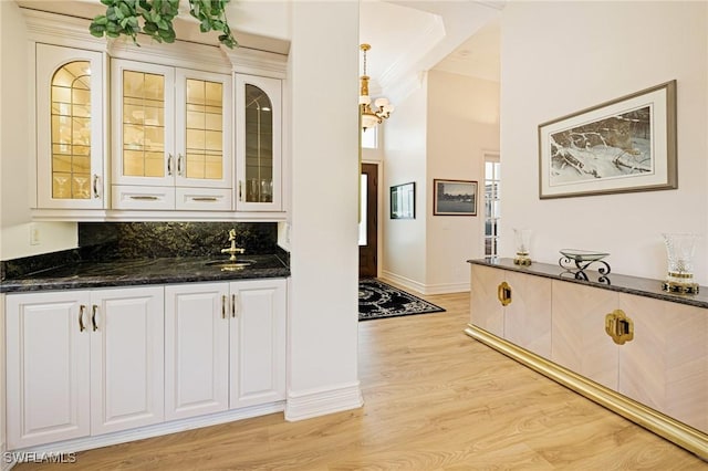 bar area with light wood-type flooring, a sink, and baseboards