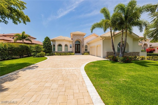 mediterranean / spanish house with stucco siding, decorative driveway, an attached garage, a front lawn, and stone siding