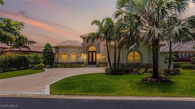 mediterranean / spanish home with stucco siding, curved driveway, a front lawn, stone siding, and a tile roof