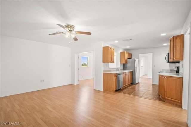 kitchen with light countertops, appliances with stainless steel finishes, a ceiling fan, and light wood finished floors