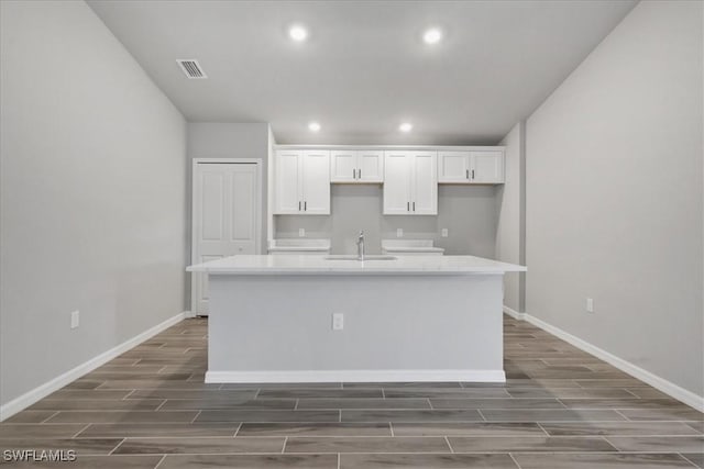 3225 58th St W, Lehigh Acres, FL 33971 - kitchen with a sink, wood tiled floor, white cabinetry, a center island with sink, and visible vents