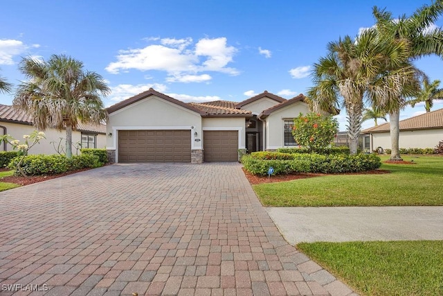mediterranean / spanish home featuring stucco siding, decorative driveway, a garage, a front yard, and stone siding