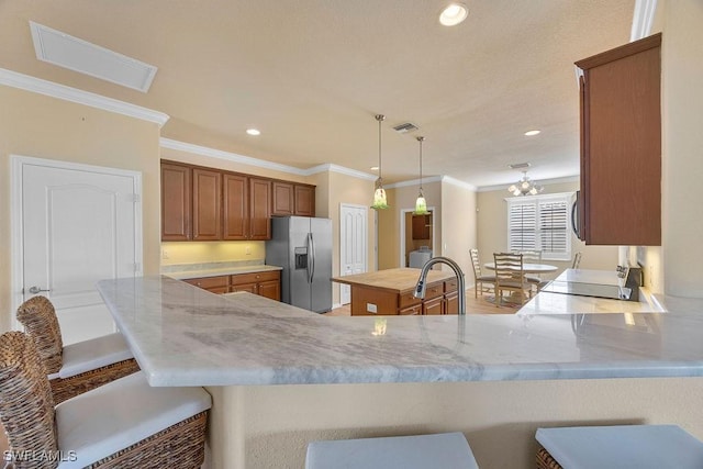 kitchen with stainless steel fridge, a breakfast bar, brown cabinetry, a peninsula, and ornamental molding