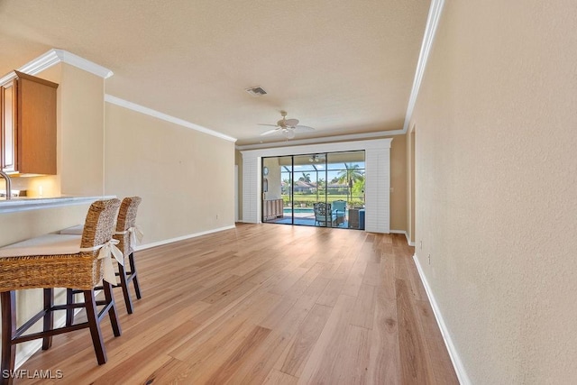 living room with ornamental molding, baseboards, light wood-style floors, and ceiling fan