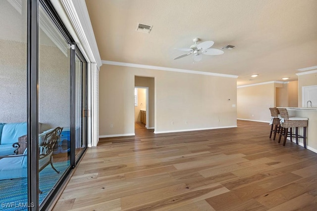 living area featuring ceiling fan, crown molding, baseboards, and light wood-type flooring