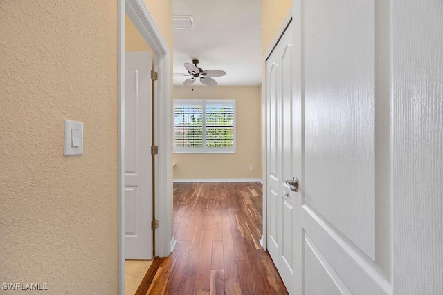 hall featuring a textured wall, wood finished floors, and baseboards