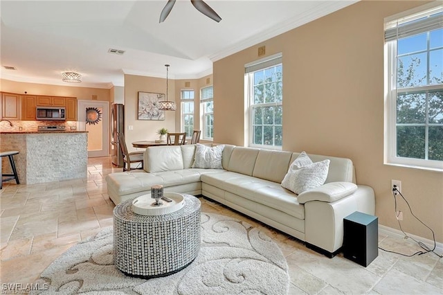 living room with stone tile floors, baseboards, visible vents, ceiling fan, and ornamental molding