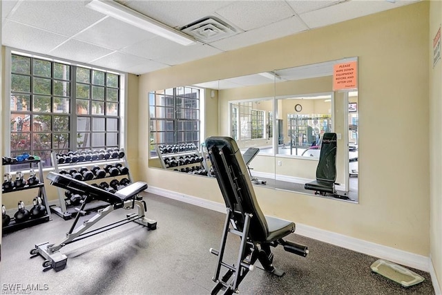 exercise room with visible vents, a drop ceiling, and baseboards