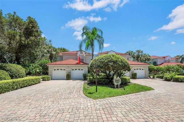 mediterranean / spanish-style home featuring decorative driveway, stucco siding, an attached garage, and a tiled roof