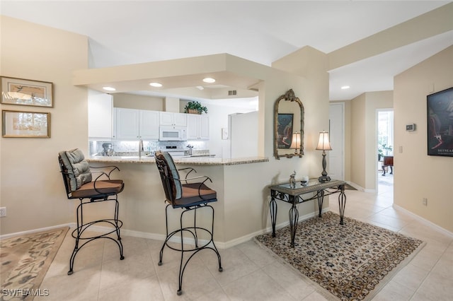 kitchen featuring white microwave, a kitchen bar, white cabinetry, light tile patterned flooring, and a peninsula