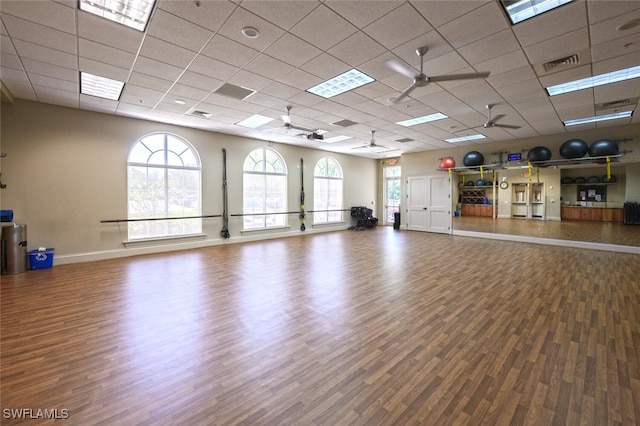 exercise area with wood finished floors, ceiling fan, a paneled ceiling, and baseboards