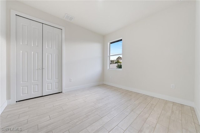 unfurnished bedroom with light wood-style flooring, a closet, baseboards, and visible vents