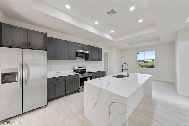 kitchen with a sink, a raised ceiling, visible vents, light stone counters, and appliances with stainless steel finishes